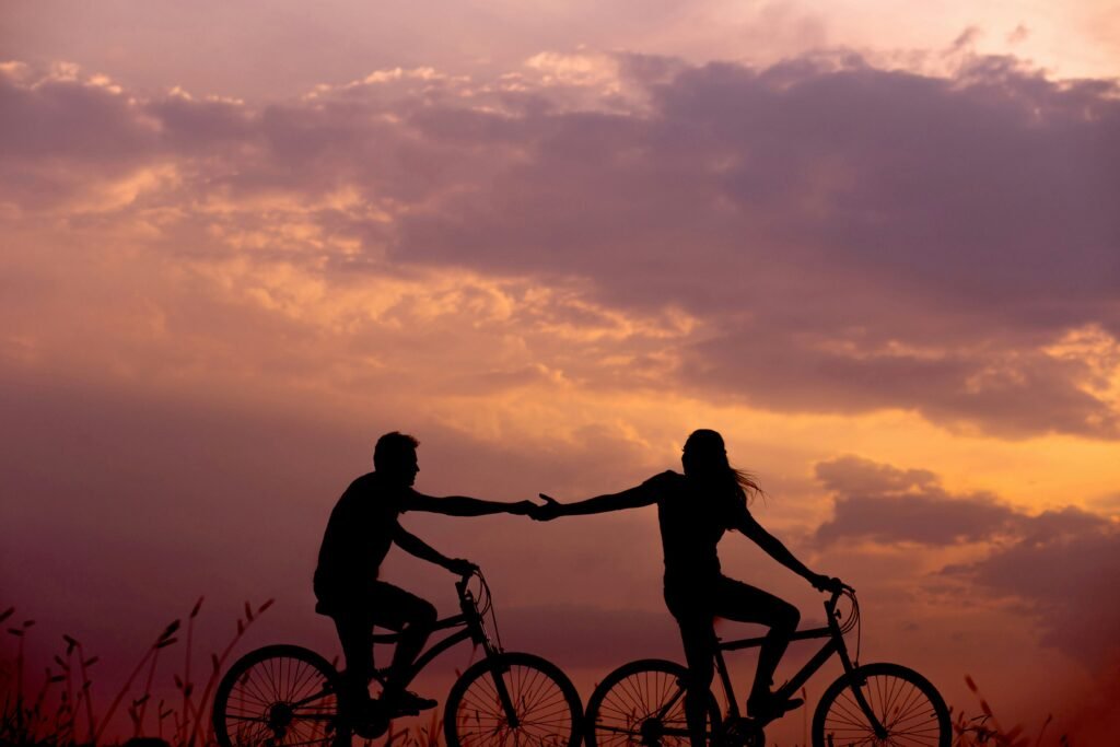 Silhouette of a couple on two bicycles holding hands.
